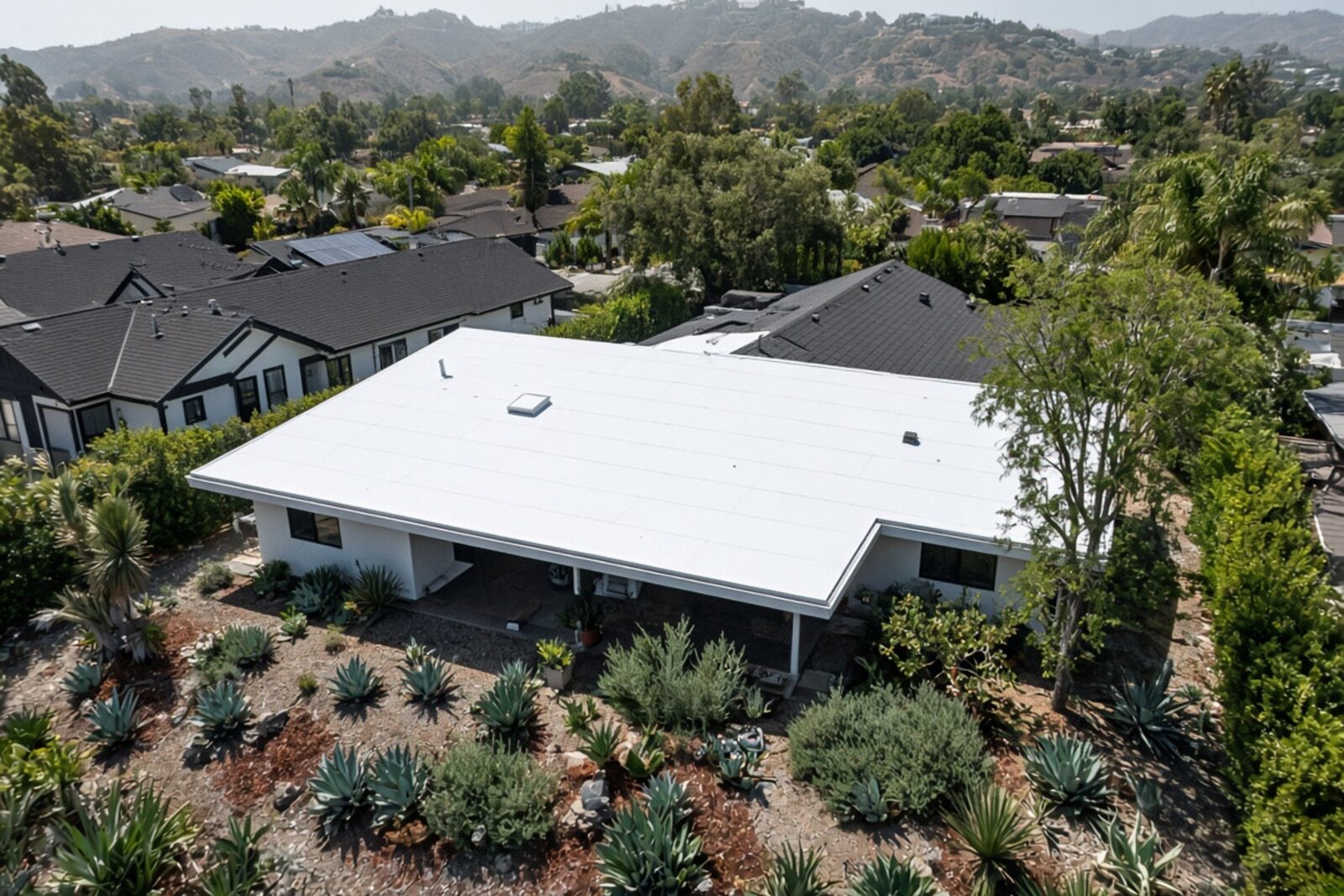 White high-reflectance cool roof on a low-slope Los Angeles home surrounded by darker neighboring roofs